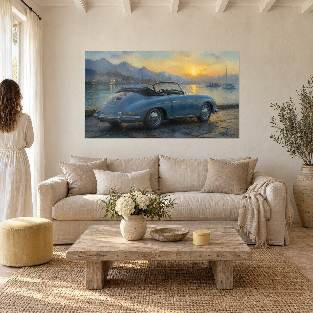 Wall art of a steel-blue convertible parked facing the orange sunset, sailboats on the water, above a sofa in a bright living room