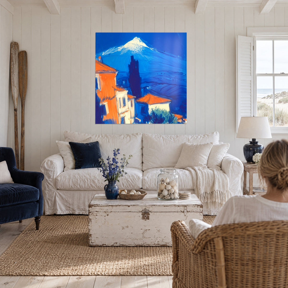 Gemälde schneebedeckter Vulkan in Kobaltblau und leuchtendem Orange, Häuser mit roten Dächern, über einem Sofa in einem hellen Wohnzimmer