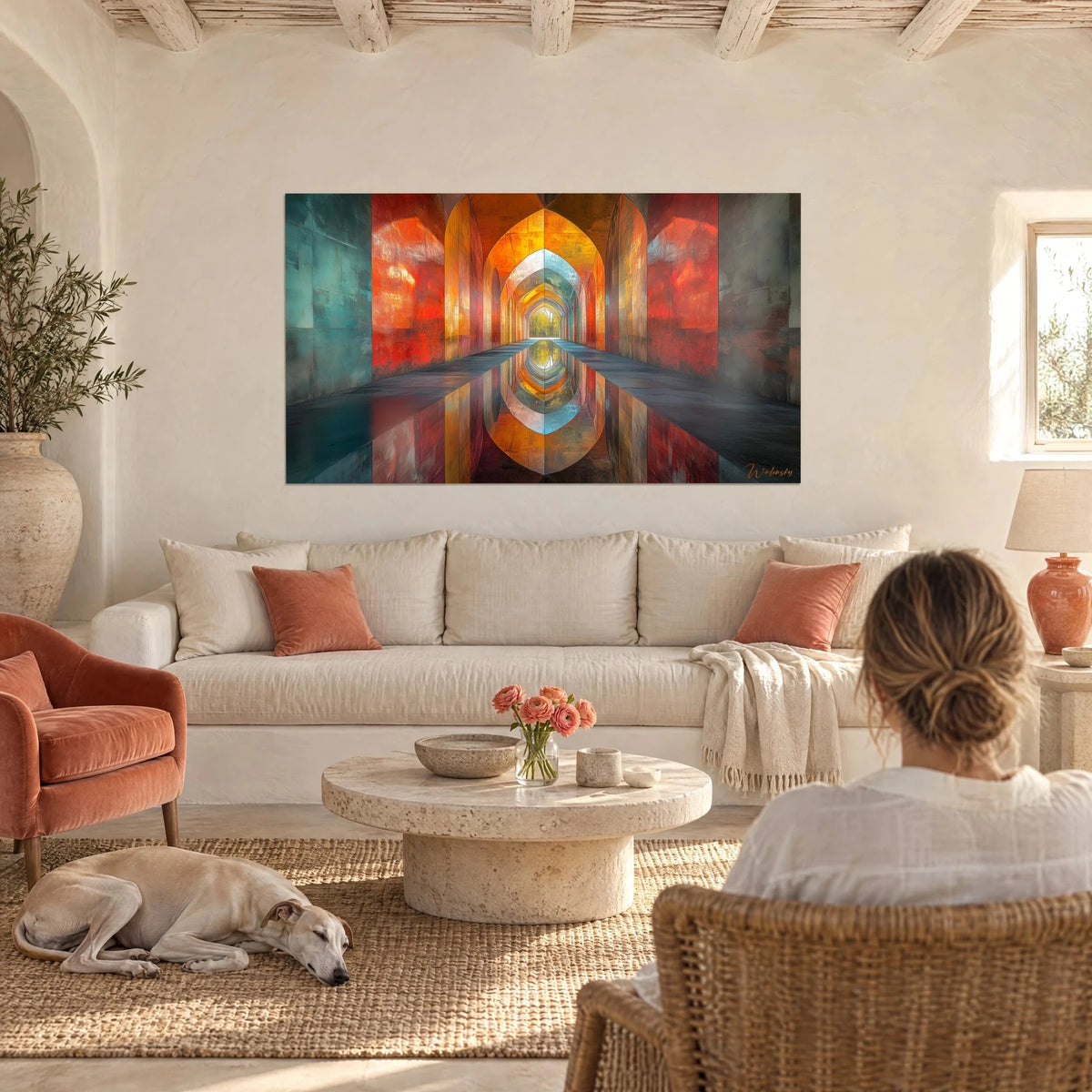 Wall art corridor of pointed arches in vermilion and amber, reflected in water, seen from behind by a woman, above a sofa in a bright living room