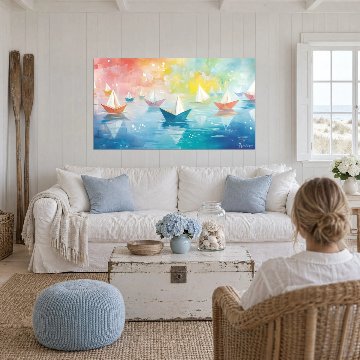 Tableau bateaux en papier plié sur eau turquoise, ciel rose et jaune, au-dessus d'un canapé dans un salon lumineux