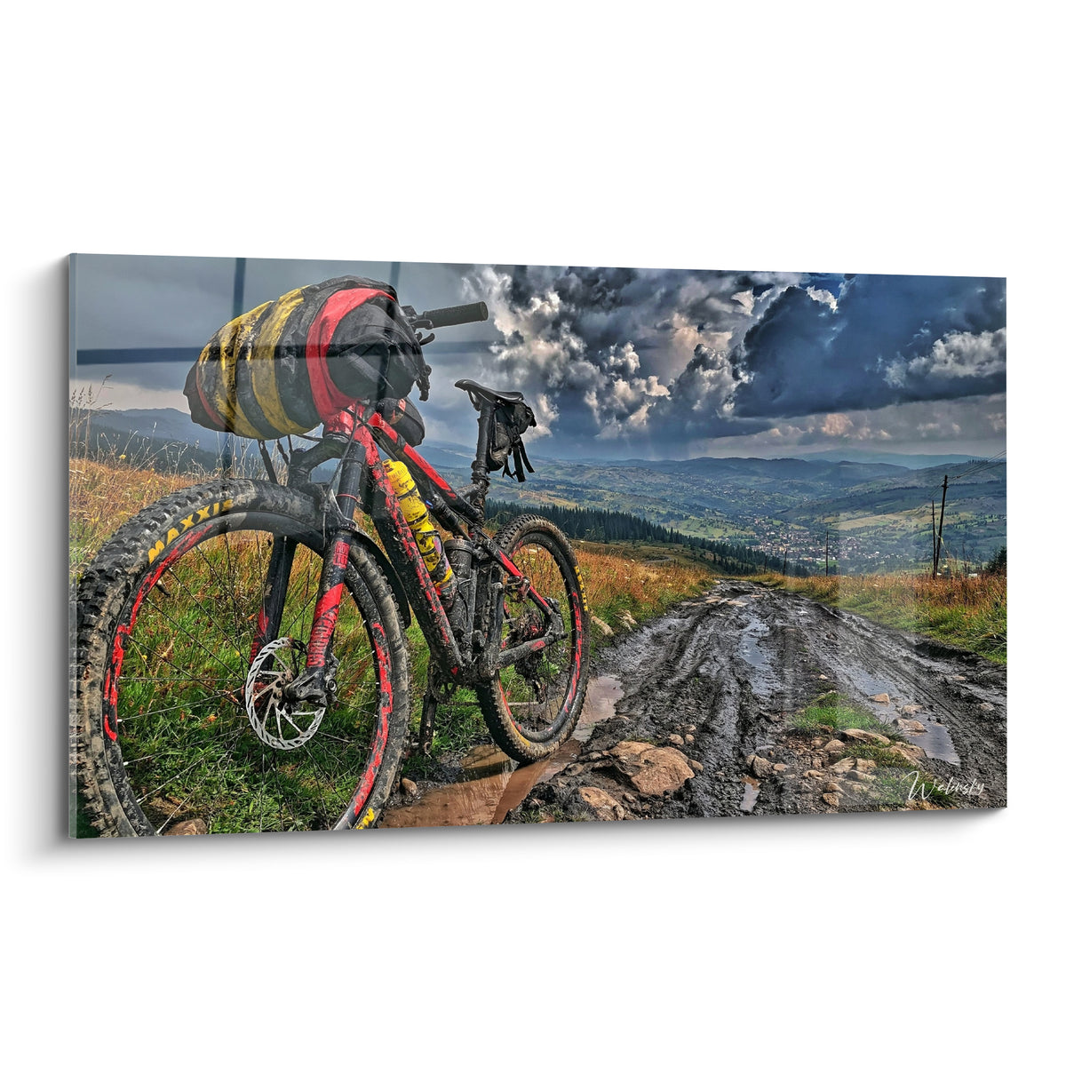 VTT rouge et noir couvert de boue, sacoche jaune, face à un ciel d'orage anthracite