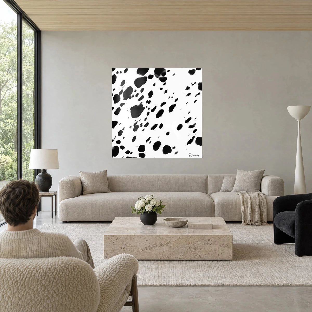 Wall art of black ink splatters falling like rain on a white background, two people seen from behind, above a sofa in a bright living room