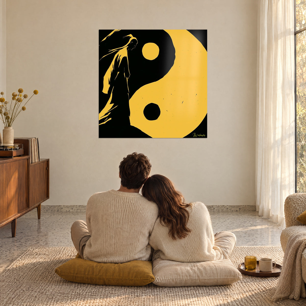 Wall art yin yang balance, black silhouette with ochre yellow strands, admired by an embracing couple on mustard cushions, bright living room