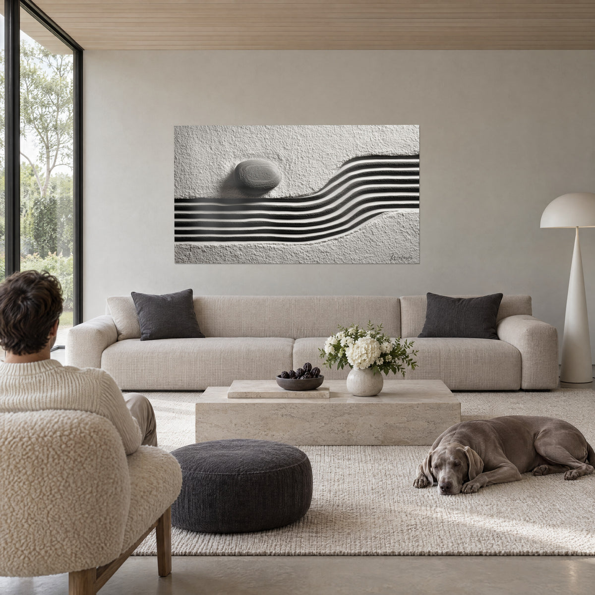 Wall art grey pebble on white sand striated with black grooves, man seen from behind and Weimaraner lying on a sofa in a bright living room