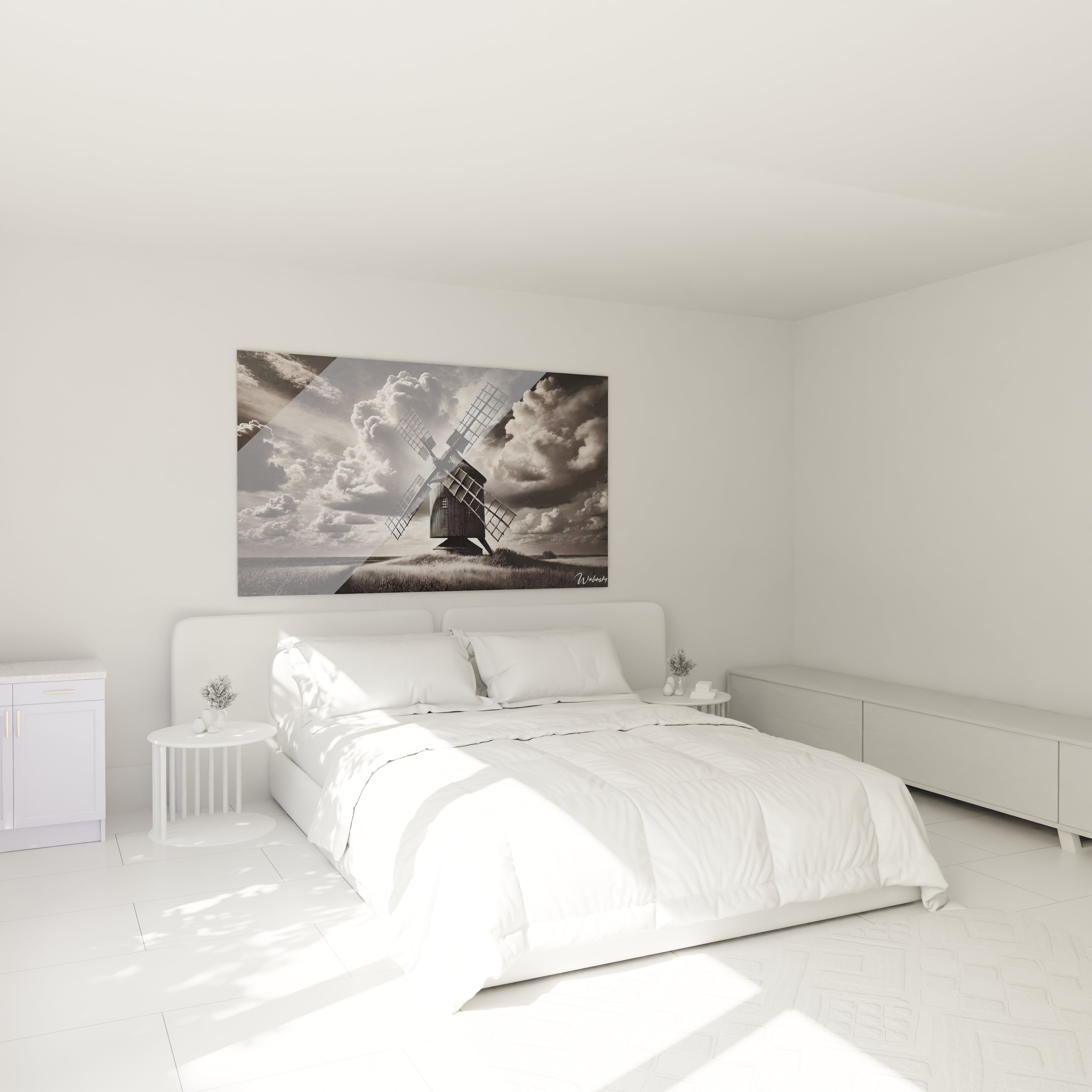 Tableau noir et blanc au-dessus du lit dans une chambre paisible capturant un moulin et des nuages lourds pour une ambiance serene et introspective.
