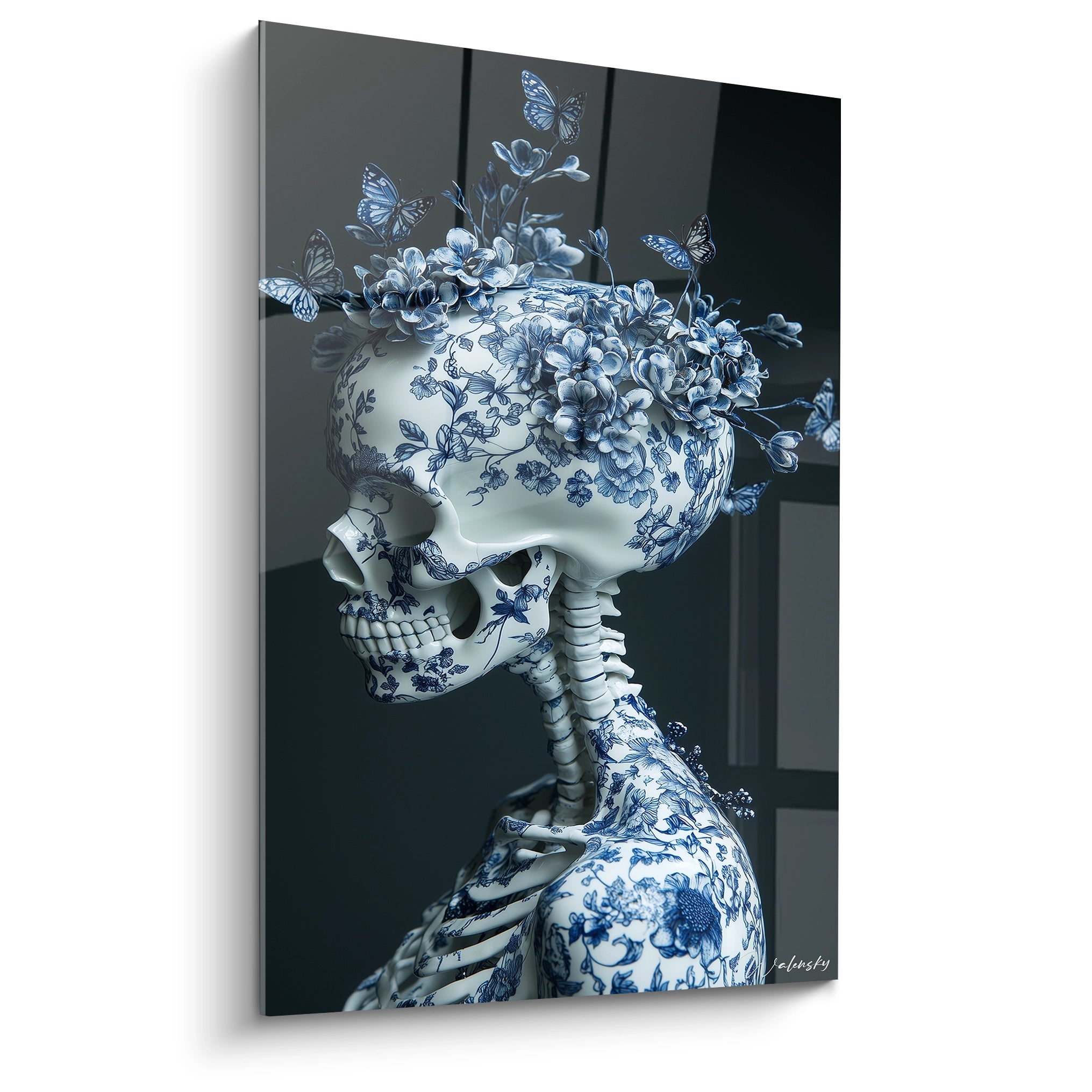Un tableau porcelaine crâne décoré de motifs floraux bleu cobalt sur fond blanc, surmonté de fleurs et papillons bleus tridimensionnels. La composition montre un crâne et une partie de cage thoracique ornés de motifs délicats, photographiés sur fond noir profond.
