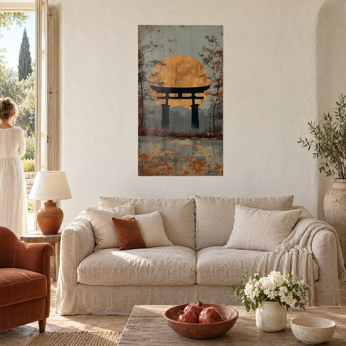 Schilderij met een zwarte torii-poort voor een immense gouden zonneschijf, roodbruin bos, gezien van achteren door een vrouw boven een bank in een lichte woonkamer