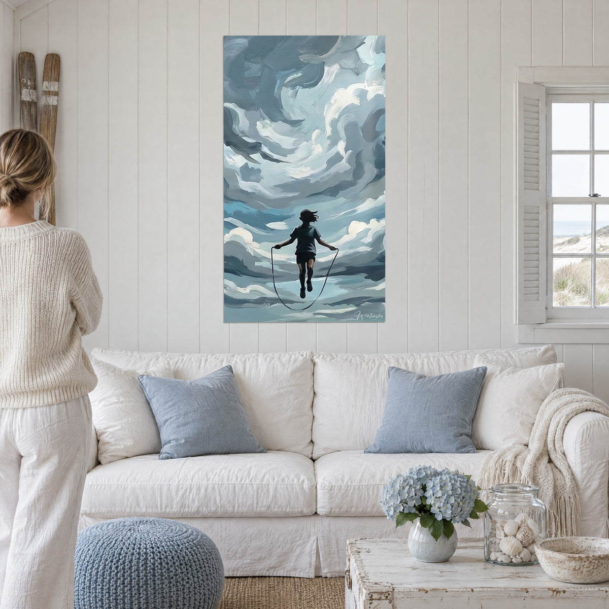 Cuadro de un niño saltando, cuerda tensa, cielo de pinceladas azul grisáceo y blancas, encima de un sofá en un salón luminoso