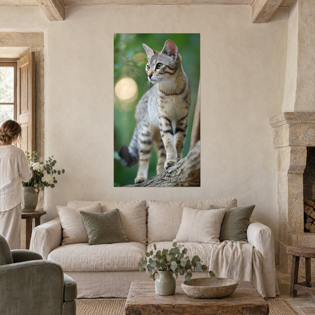 Gemälde Tigerkatze mit grünen Augen auf einem Ast sitzend, grüner Hintergrund mit goldenem Bokeh, zwei Personen von hinten über einem Sofa in einem hellen Wohnzimmer