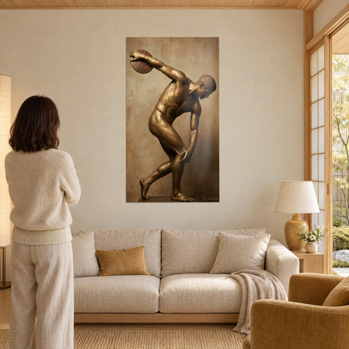 Wall art bronze discus thrower in full motion, copper-toned body on sand background, woman seen from behind, above a sofa in a bright living room