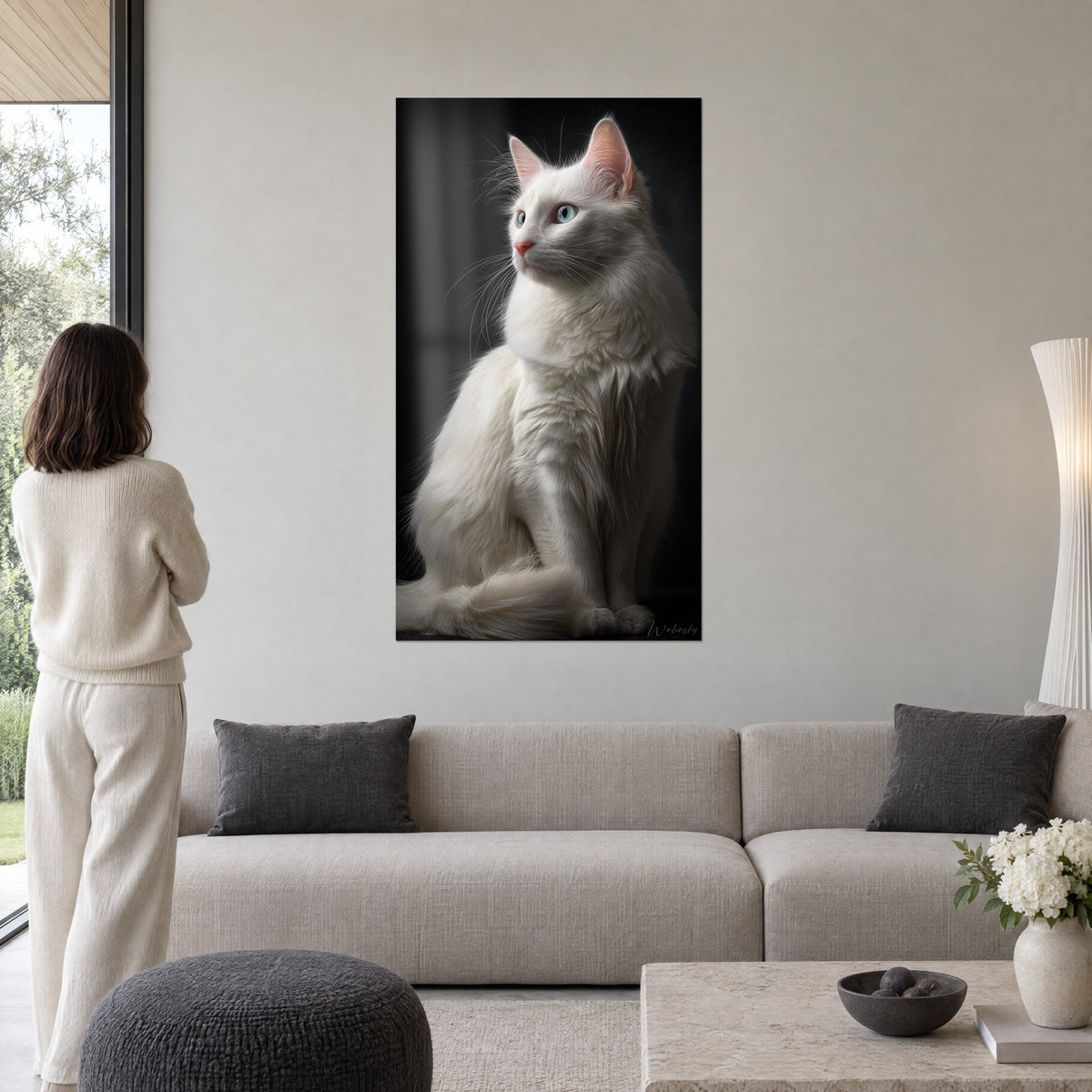 Πίνακας λευκή γάτα angora με μάτια γαλαζοπράσινα σαν παγετώνας, χιονόλευκη γούνα σε μαύρο φόντο, γυναίκα από πίσω πάνω από έναν καναπέ σε φωτεινό σαλόνι