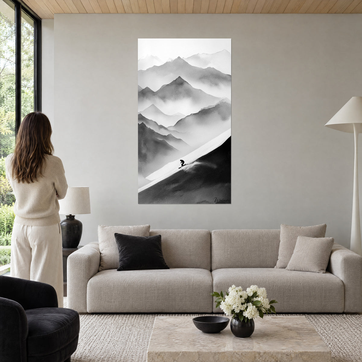 Wall art of a snowboarder as a black silhouette racing down a white slope, misty grey ridges, above a sofa in a bright living room