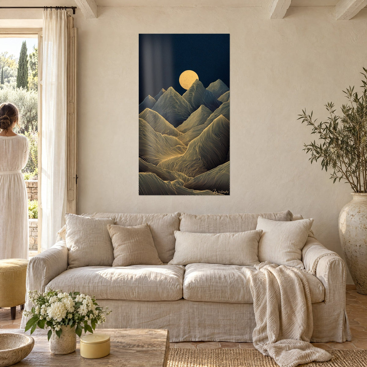 Cuadro montañas con líneas doradas bajo una luna ocre, fondo azul noche, una mujer de espaldas sobre un sofá en un salón luminoso