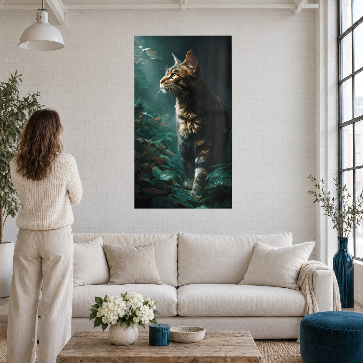 Gemälde Getigerte Katze mit bernsteinfarbenen Augen, die den Wald beobachtet, dunkelgrünes Laub, Besucherin von hinten, über einem Sofa in einem hellen Wohnzimmer