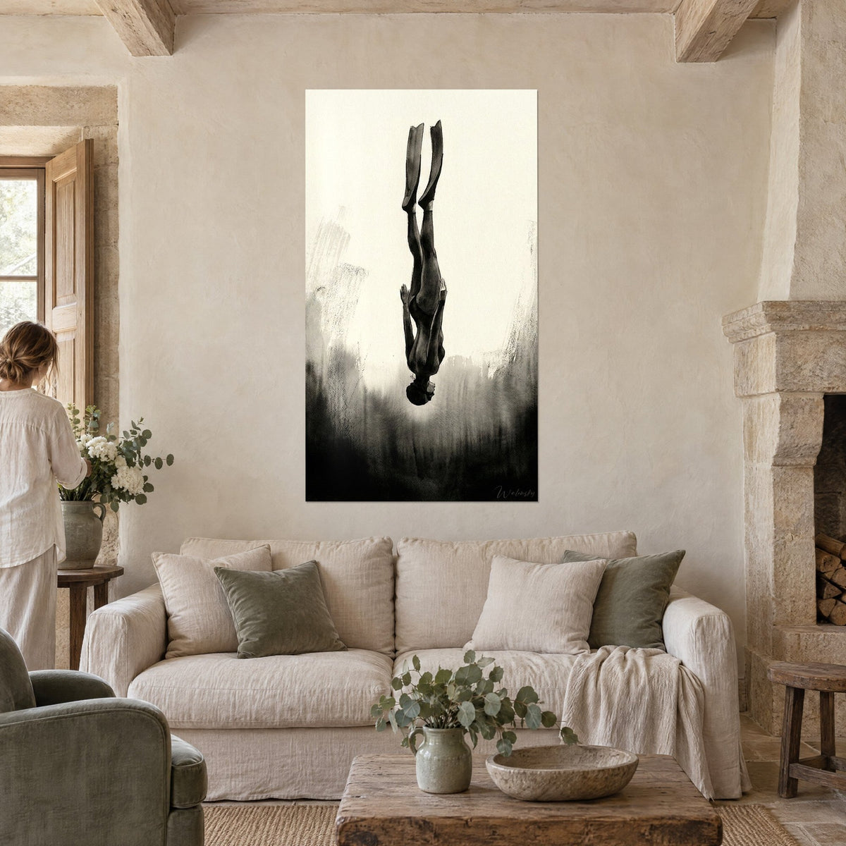 Wall art upside-down freediver, black fins reaching toward a cream sky, grey ink, woman seen from behind above a sofa in a bright living room