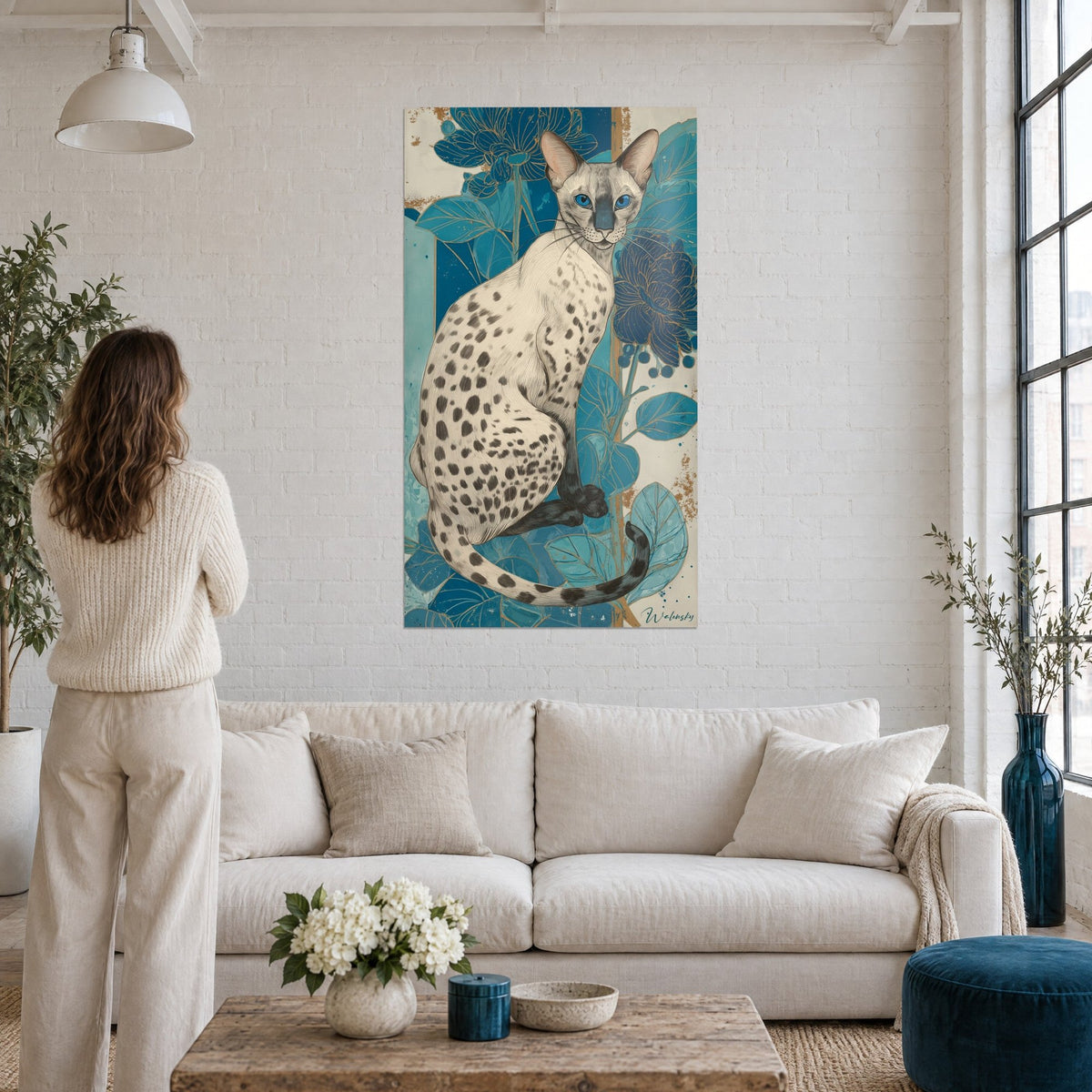 Gemälde Serengeti-Katze mit blauen Augen und Fleckenzeichnung, indigoblaue Blüten und türkisfarbene Blätter, über einem Sofa in einem hellen Wohnzimmer
