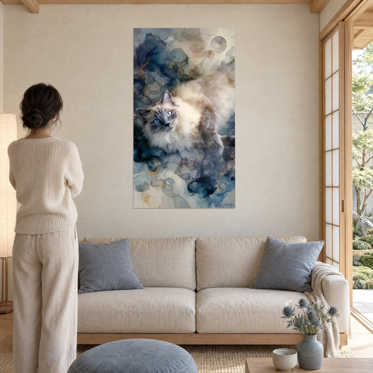 Gemälde Ragdoll-Katze mit blauen Augen, liegend auf indigoblauen und goldenen Tintenwolken, über einem Sofa in einem hellen Wohnzimmer