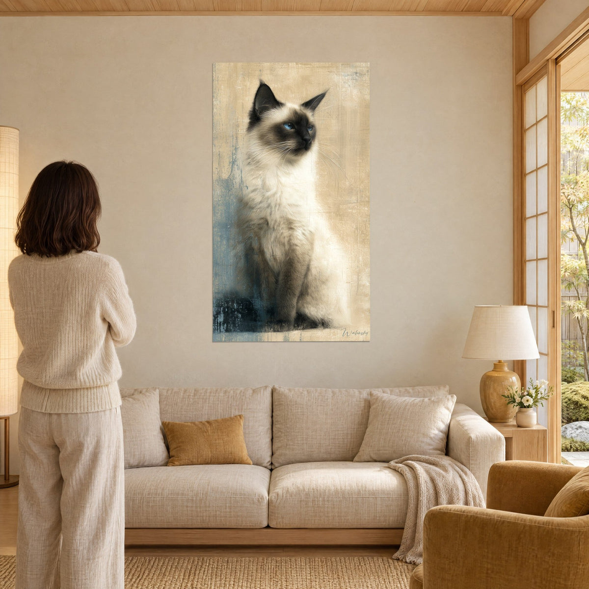 Schilderij Birmaanse kat met saffierblauwe ogen, crèmekleurige vacht en bruin masker, zijdelingse blik, een vrouw van achteren, boven een bank in een lichte woonkamer