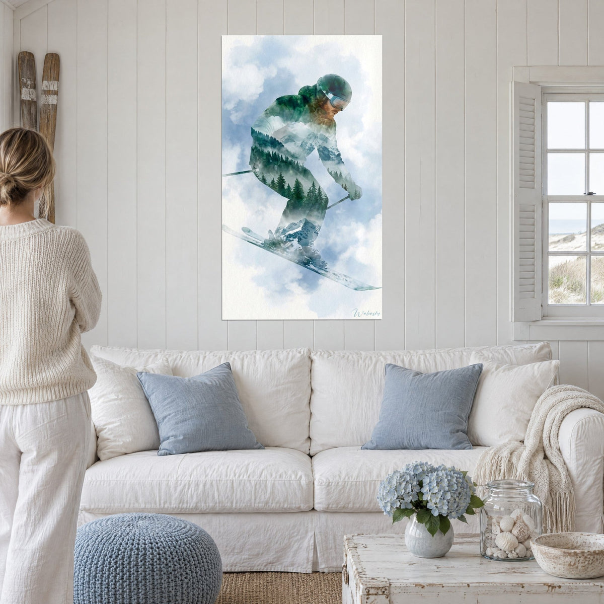 Tableau skieur en double exposition, forêt de sapins verts et sommets bleutés dans un ciel nuageux, au-dessus d'un canapé dans un salon lumineux