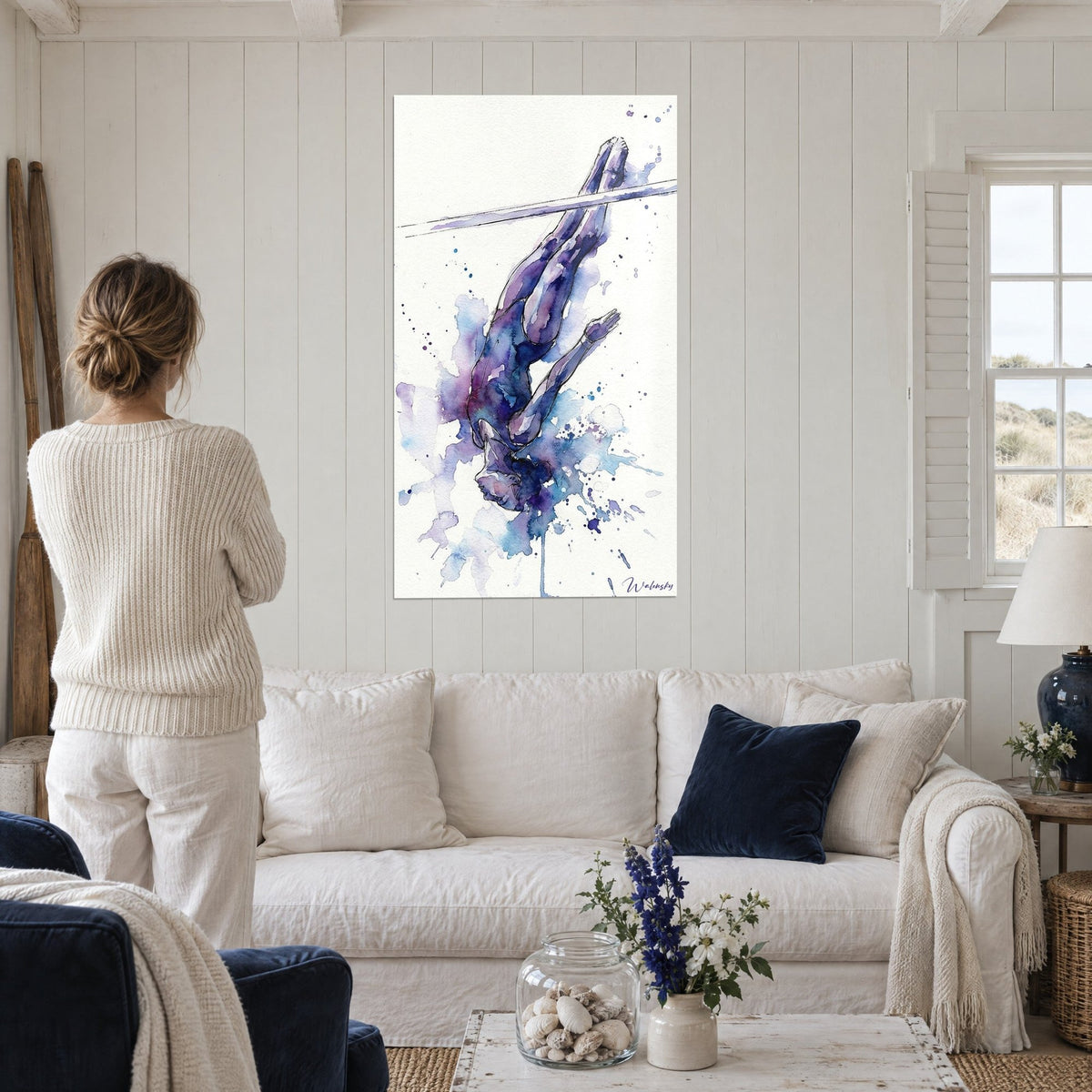 Wall art gymnast in a watercolor dive, purple and turquoise body above a bar, hanging above a sofa in a bright living room