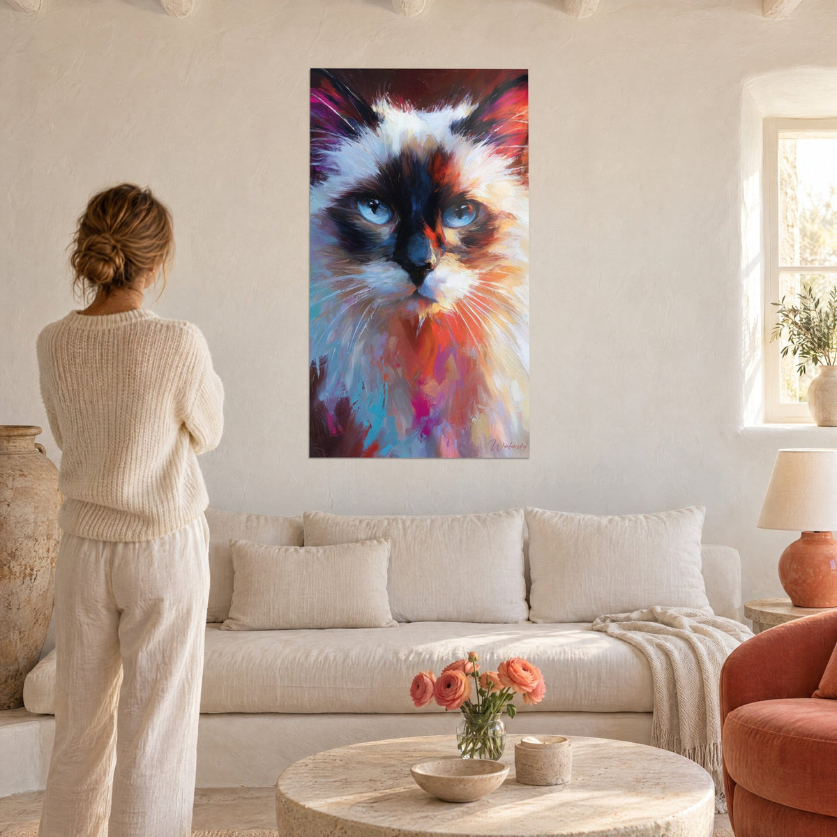 Schilderij Birmaanse kat met blauwe ogen, bruin masker en crèmekleurige vacht met oranje spatten, vrouw van achteren, boven een bank in een lichte woonkamer