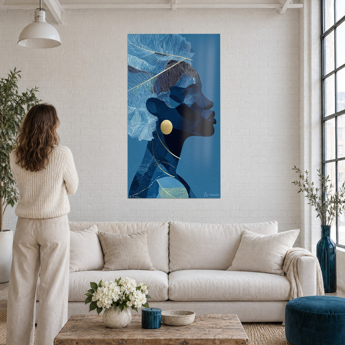 Wall art profile of a woman in midnight blue with frosted feathers and a golden curl, above a sofa in a bright living room