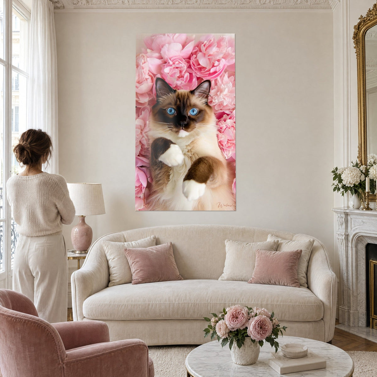 Schilderij Birmaanse kat met blauwe ogen opgekruld tussen roze en crème pioenrozen, boven een bank in een lichte woonkamer