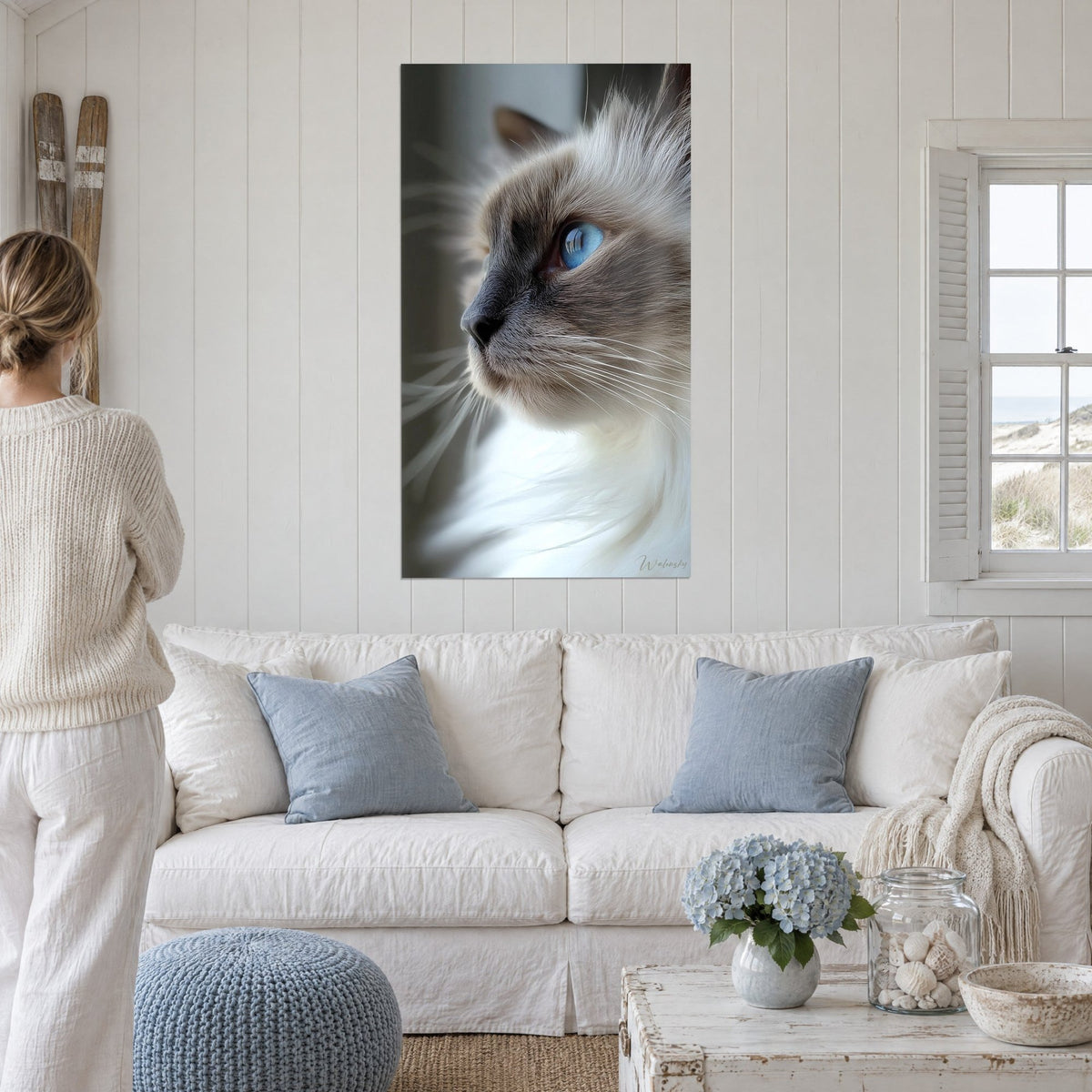 Tableau chat Birman de profil aux yeux bleus, pelage crème et museau gris, deux personnes de dos, au-dessus d'un canapé dans un salon lumineux
