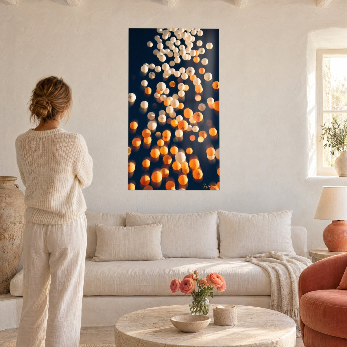 Wall art with white and orange ping-pong balls falling against a midnight blue background, above a sofa in a bright living room