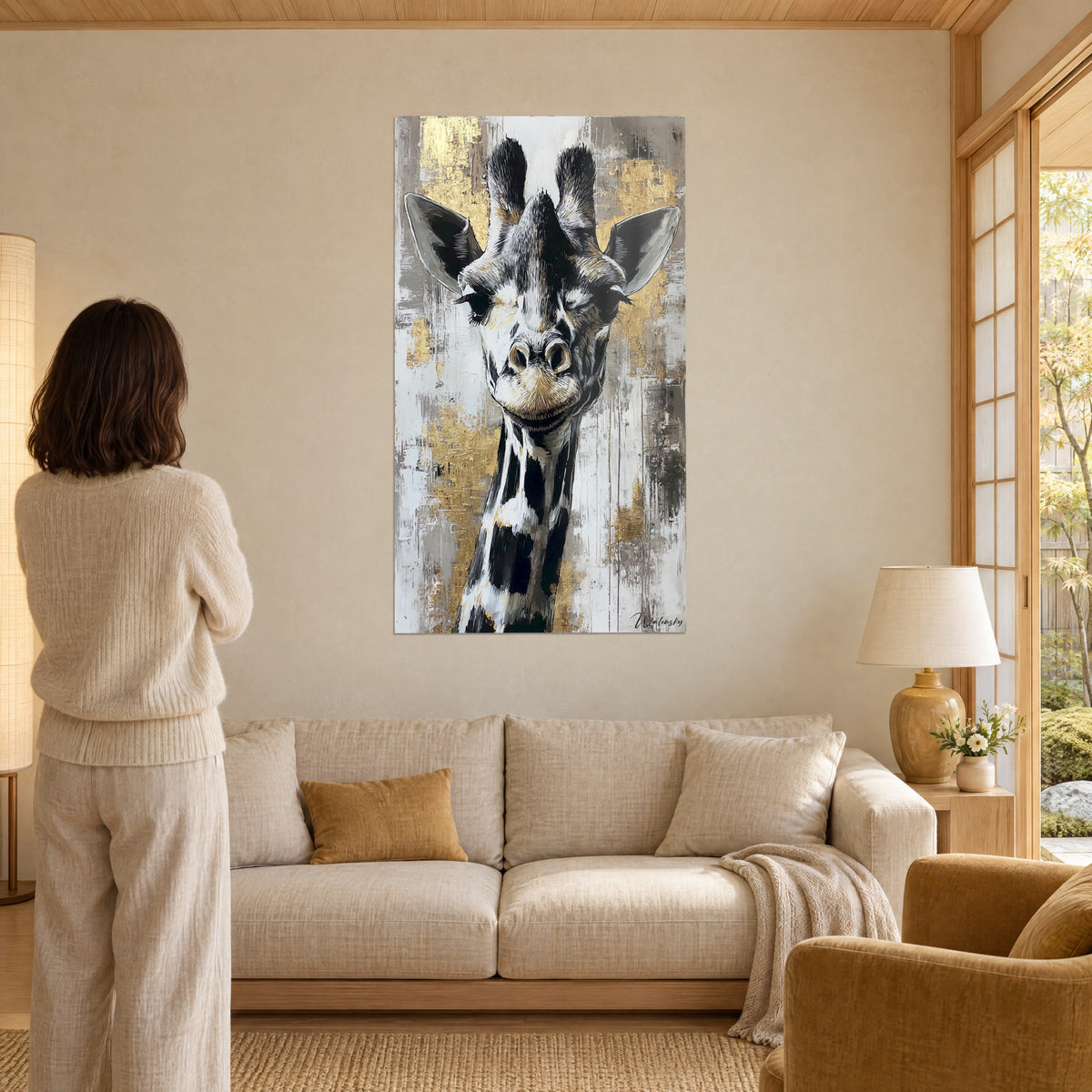 Tableau girafe au regard malicieux, pelage noir et blanc sur fond de feuilles d'or, femme de dos, au-dessus d'un canapé dans un salon lumineux