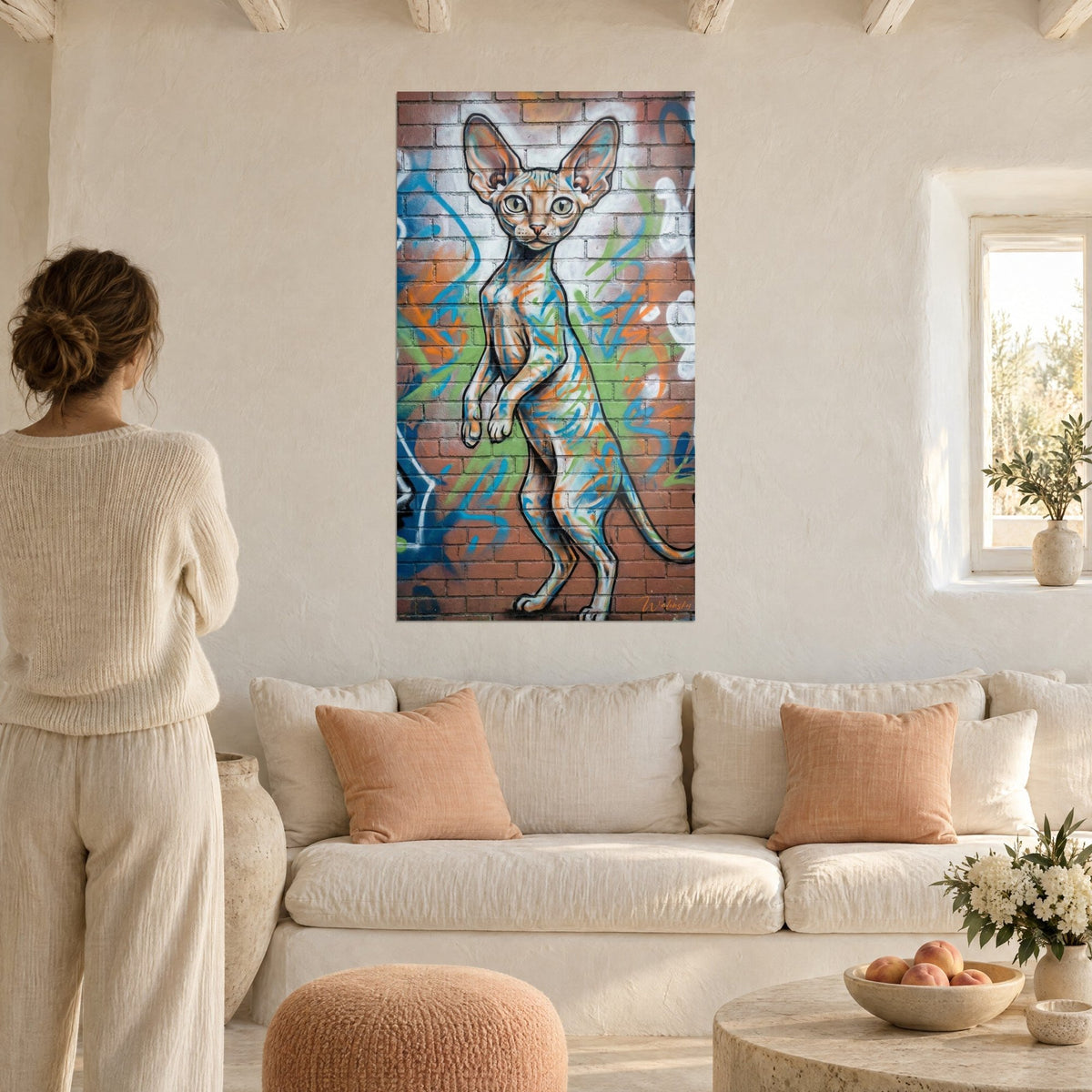 Quadro gatto Cornish Rex ritto sulle zampe posteriori, orecchie grandi, sfondo di mattoni rossi con tratti blu, sopra un divano in un soggiorno luminoso