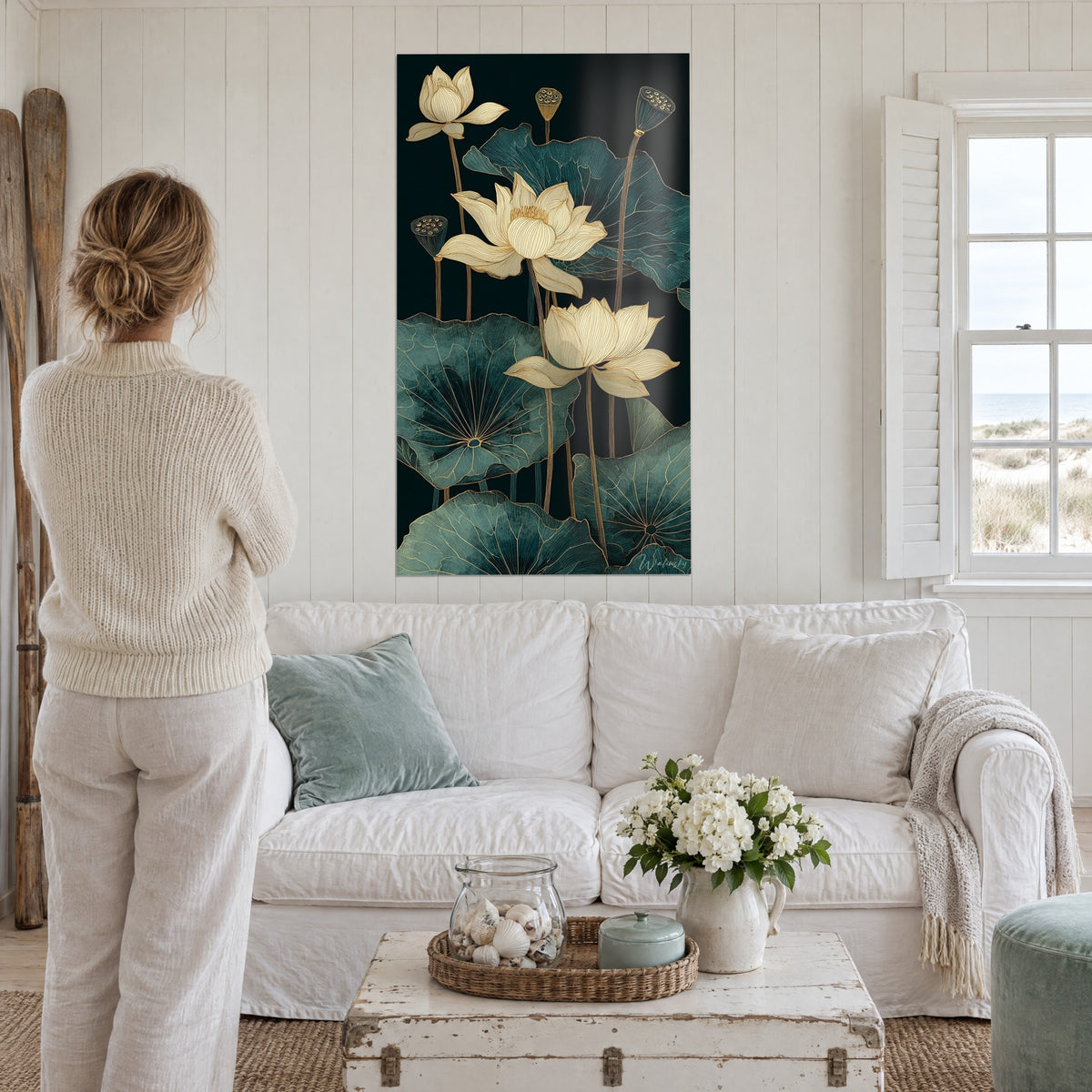 Tableau fleurs de lotus crème aux fines lignes dorées sur fond noir, feuilles vert canard, femme de dos, au-dessus d'un canapé dans un salon lumineux