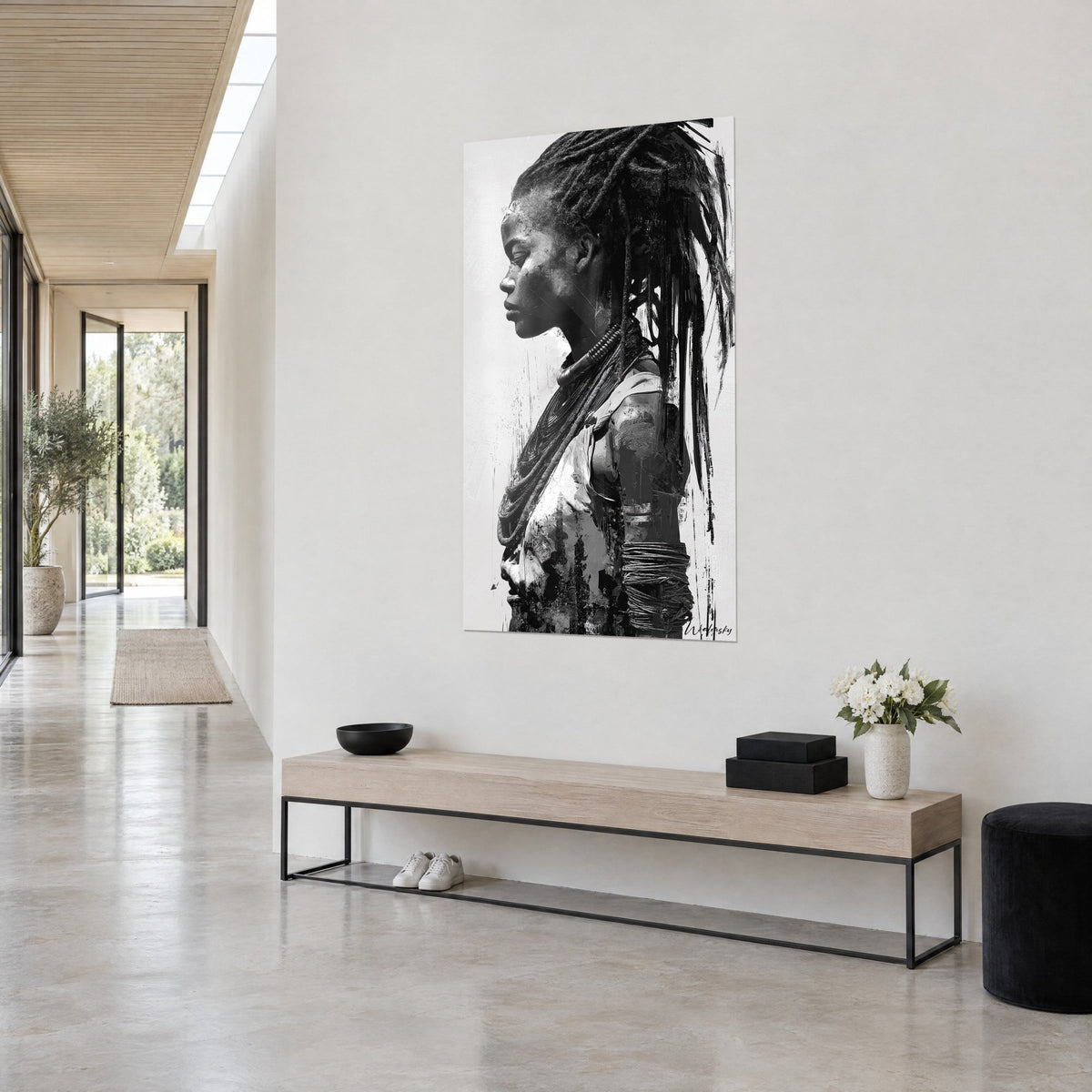 Cuadro retrato en negro y gris de una joven africana de perfil, collares de perlas y torque, colgado en una pared blanca de entrada